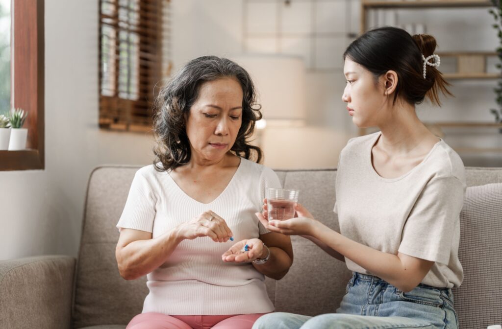 A senior woman taking medicines while her granddaughter helps her with a glass of water.