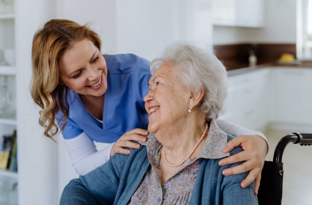 A smiling female caregiver in a blue uniform shares a warm moment with an older woman.
