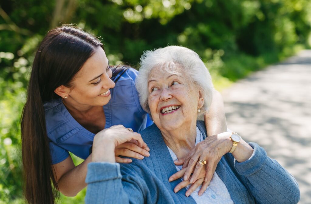 A nurse leans over the shoulder of a senior, connecting through physical touch while taking the senior outdoors for a walk