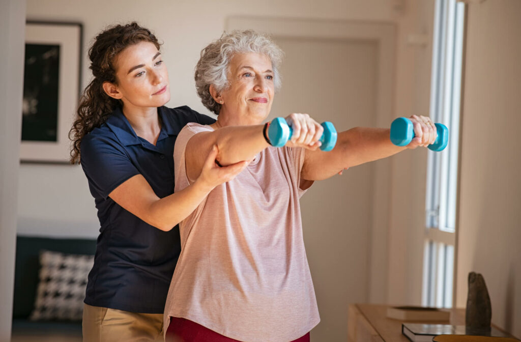 A caregiver helping an older resident lift small weights during physical therapy in skilled nursing.