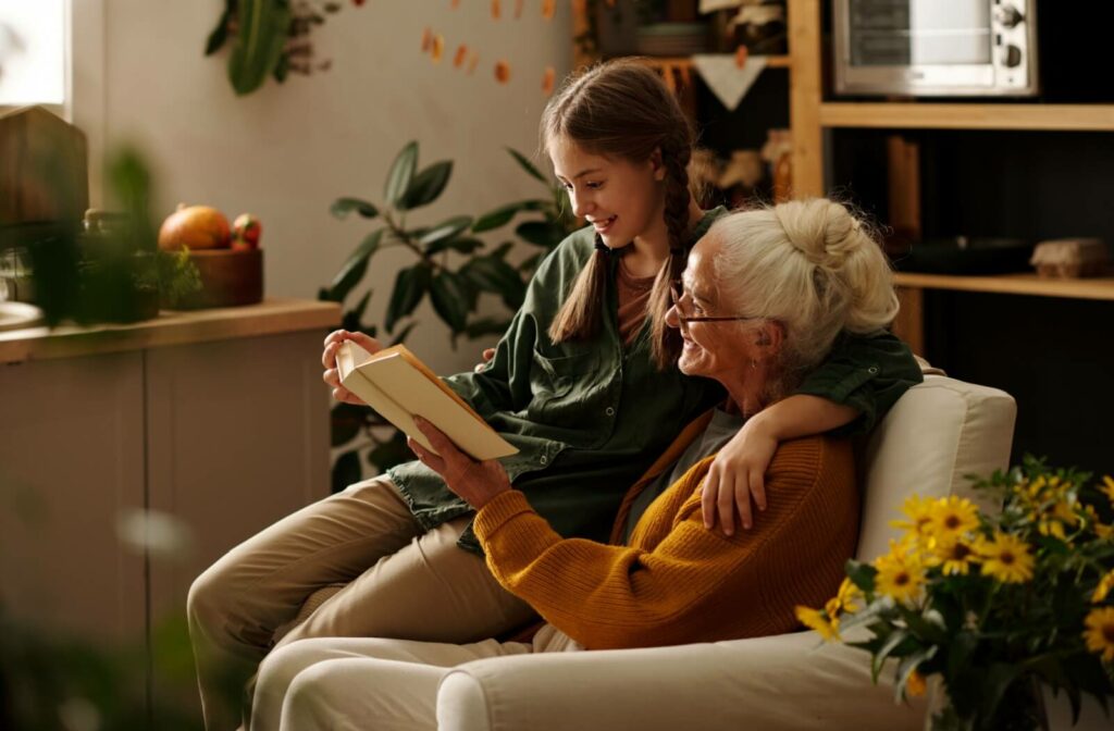 A senior reads a book alongside an older grandchild, cuddled up next to them in their warm assisted living home