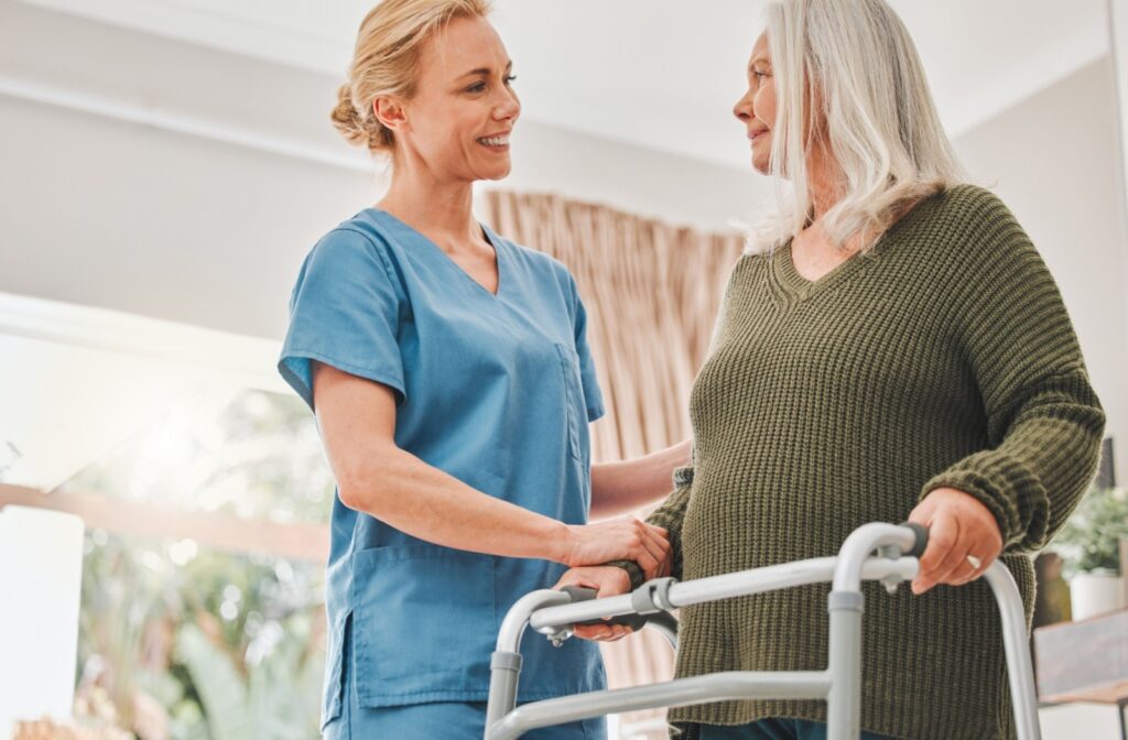 A female caregiver assisting an elderly woman stand up with a walker.