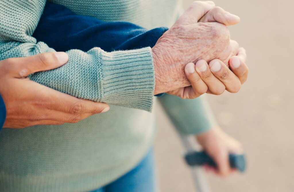 A close up of a young caregivers arms holding an elderly person's arms to offer them support as they walk.